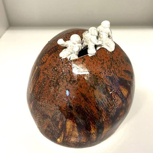 Keramisk skulptur med tre små menneskefigurer på en rund, rustik keramikbold.