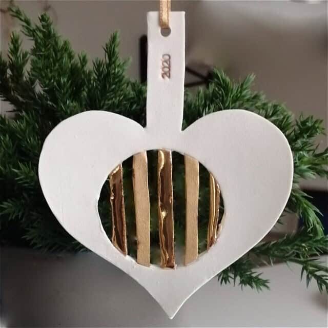 Hjerteformet julepynt med guldstriber, hængende på gran.