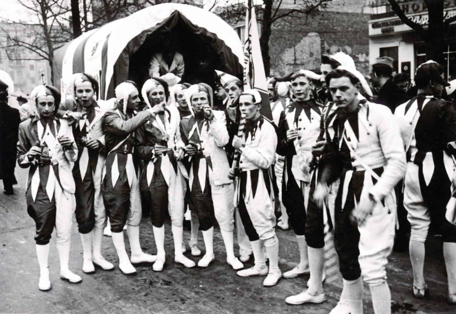 Vereinsmitglieder der KG Uhu in Harlekin-Kostümen beim Karnevalsumzug, historische Aufnahme