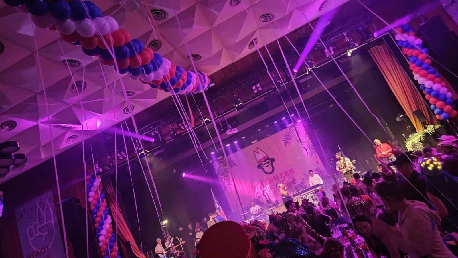 Festsaal mit lila Beleuchtung, Luftballon-Dekoration und Bühne bei einer Karnevalsveranstaltung