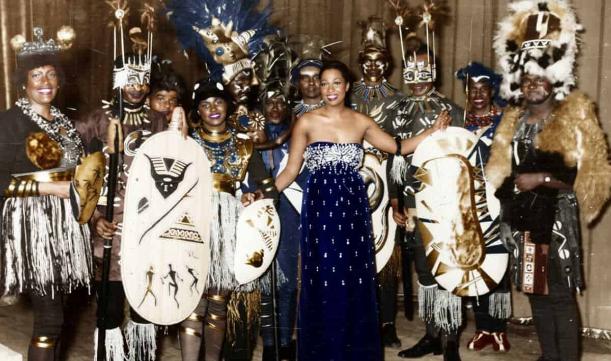 Josephine Baker in Abendkleid, umgeben von Tänzern in traditionellen afrikanischen Kostümen