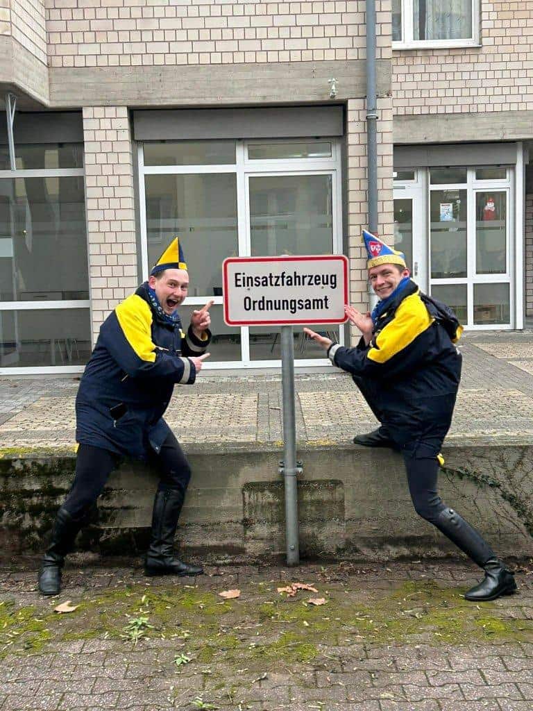 Zwei Kostümierte beim Tanzkorps posieren mit Ordnungsamt-Schilder.