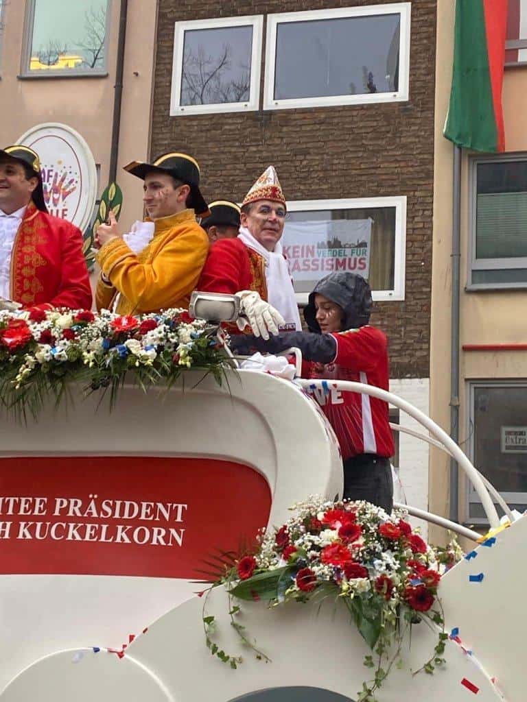Bunte Karnevalsgruppe auf einem Wagen mit Blumen, Kostümen und Narrenkappen bei der Session.