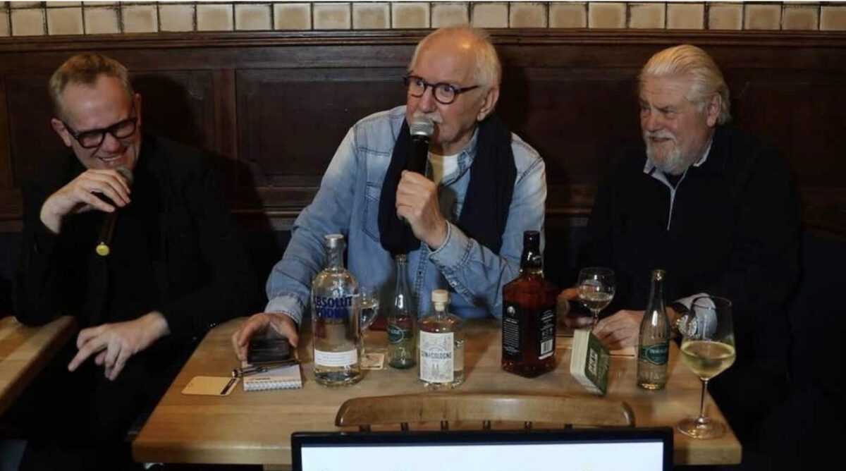 Drei Männer sitzen mit Mikrofonen an einem Tisch mit Getränken, Podcast-Aufnahme
