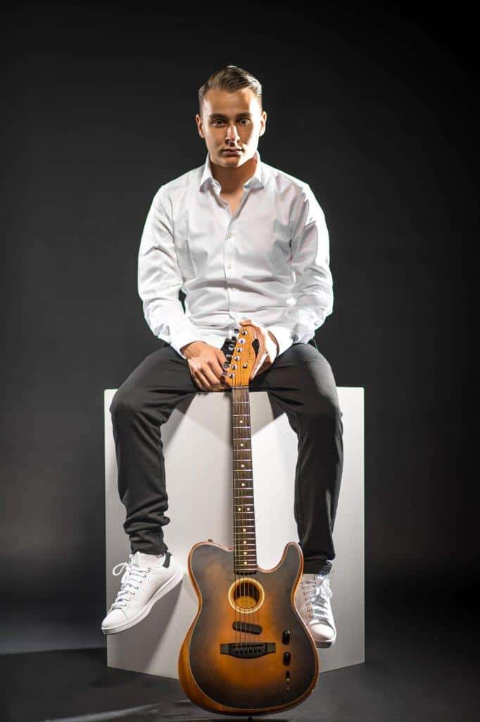 Mann sitzt mit einer E-Gitarre auf einem weißen Würfel im Fotostudio