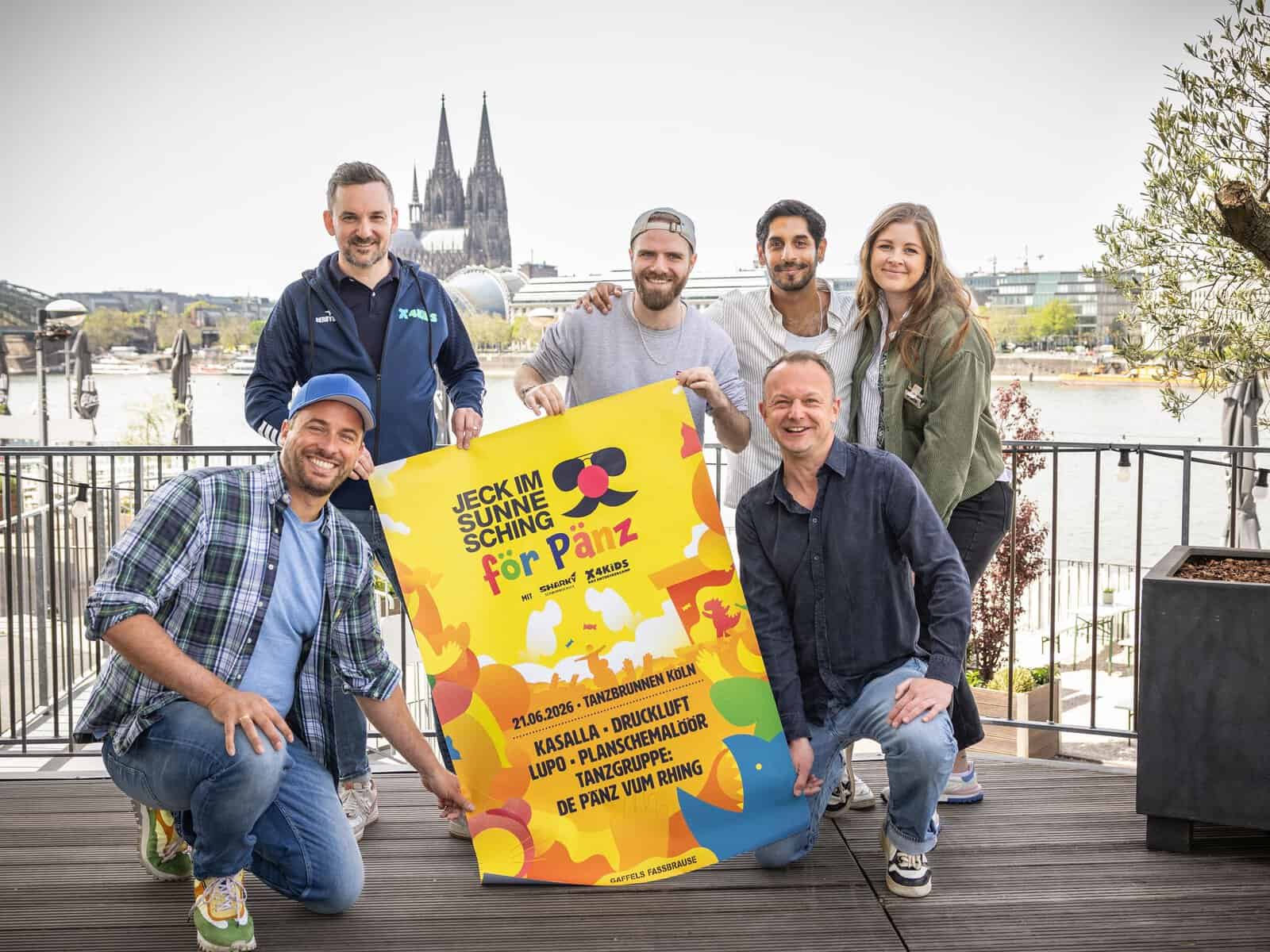 Martin Becker, Björn Lindert, Benni Landmann, Juri Rother, Jochen Gasser und Sally Halbritter präsentieren das Plakat „Jeck im Sunnesching för Pänz" vor dem Kölner Dom