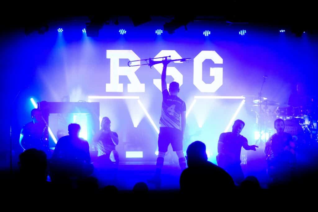 Musiker der Rhythmussportgruppe hält eine Posaune hoch auf der Bühne