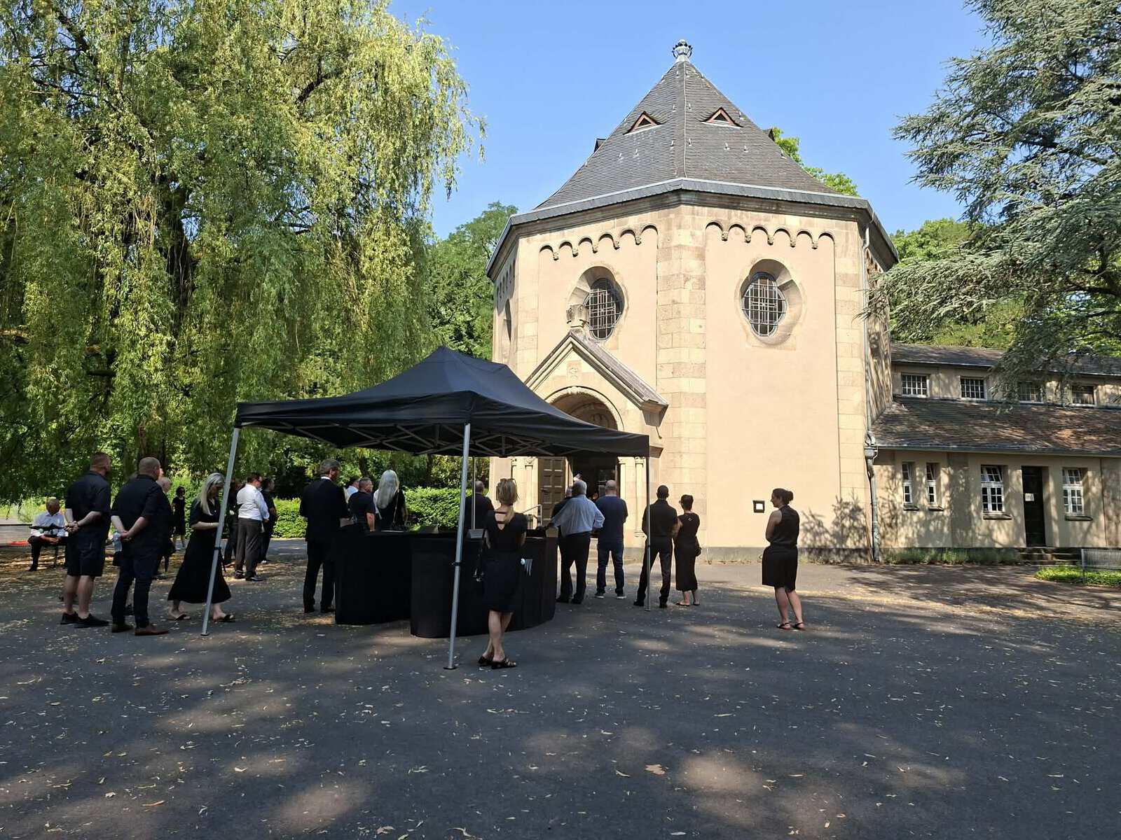 Trauergäste in schwarzer Kleidung vor einer Kapelle