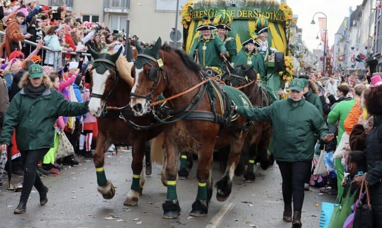 Zwei Pferde ziehen einen Festwagen der Ehrengarde der Stadt Köln durch eine Menschenmenge beim Rosenmontagszug