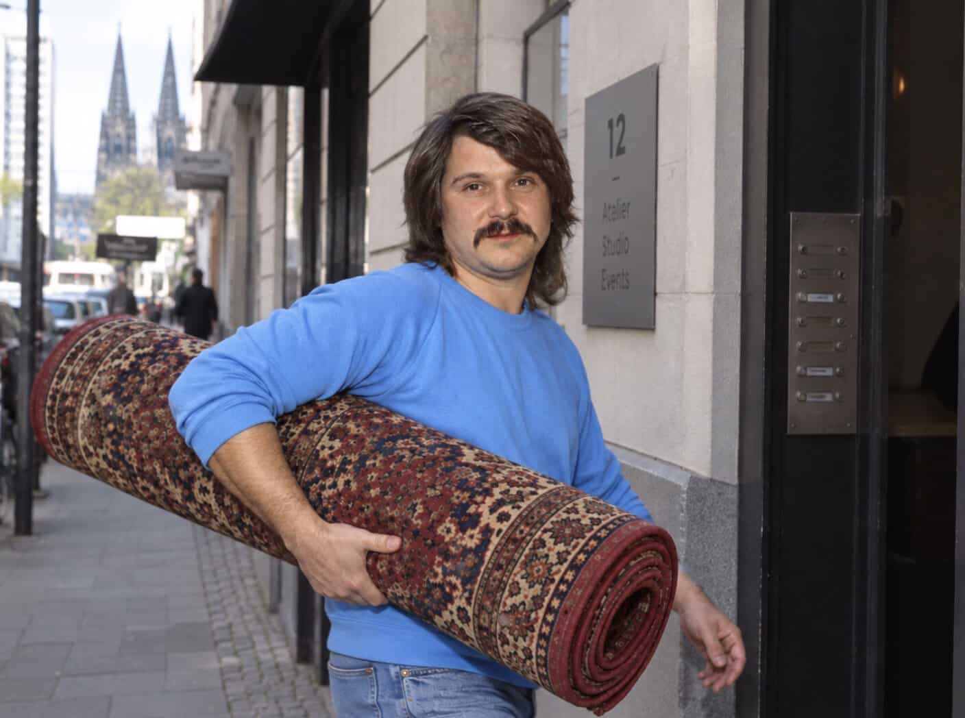 Tommy Engel trägt einen Teppich unter dem Arm und geht zum Vorsingen