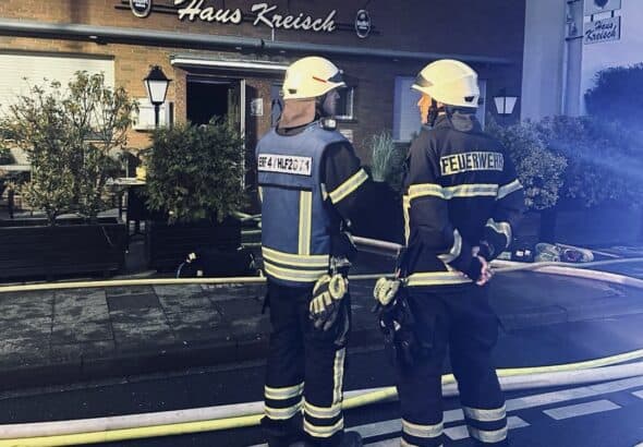 Zwei Feuerwehrleute mit Schläuchen vor der Kneipe „Haus Kreisch" bei Nacht