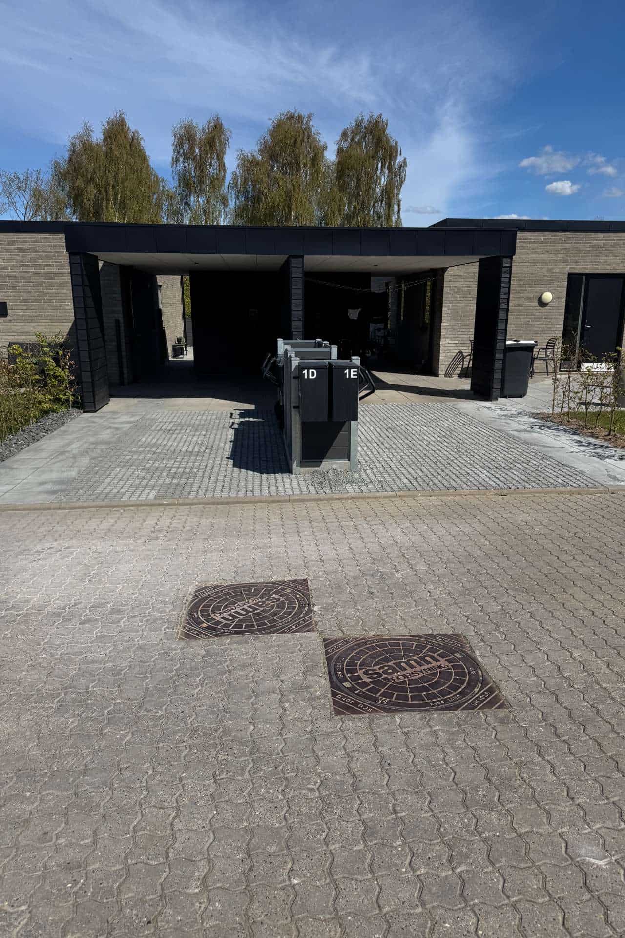 Bred fliseindkørsel der fører op til en to sorte carporte