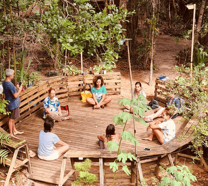 People meditating and discussing in a circular wooden outdoor space in a forest.
