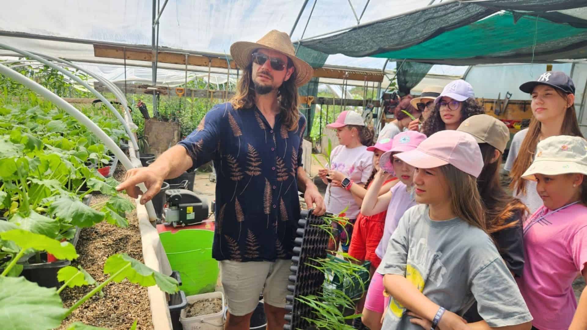 Group of children and adults learning in a greenhouse at EcoVillage.