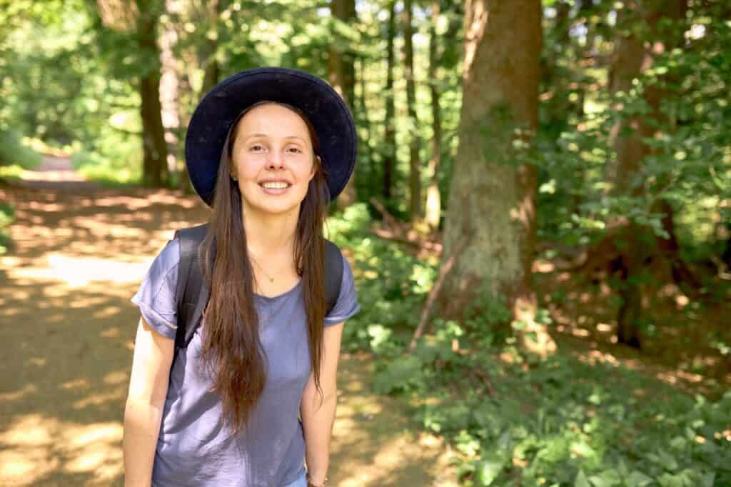 Young woman smiling in forest with trees and sunlight, eco village environment.