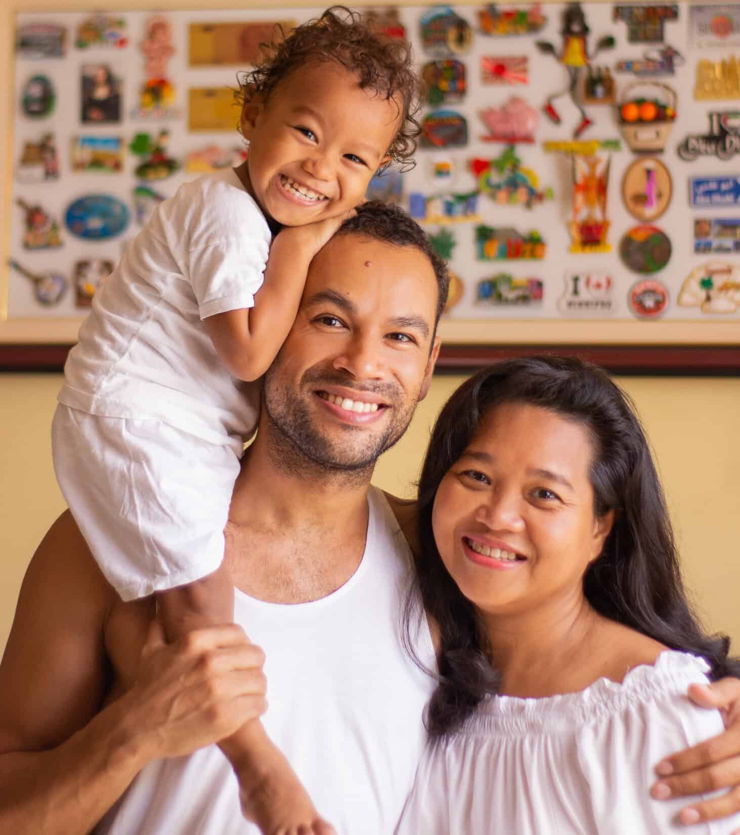 Happy family with child on father's shoulders in Ecovillage setting.