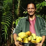 Smiling man holding a bowl of fresh apples in a lush green garden.