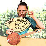 Man with sunglasses holding a sign that says 'Make compost not war' and a guitar.