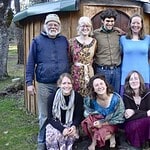 Group of diverse people smiling in front of eco-friendly round wooden structure.