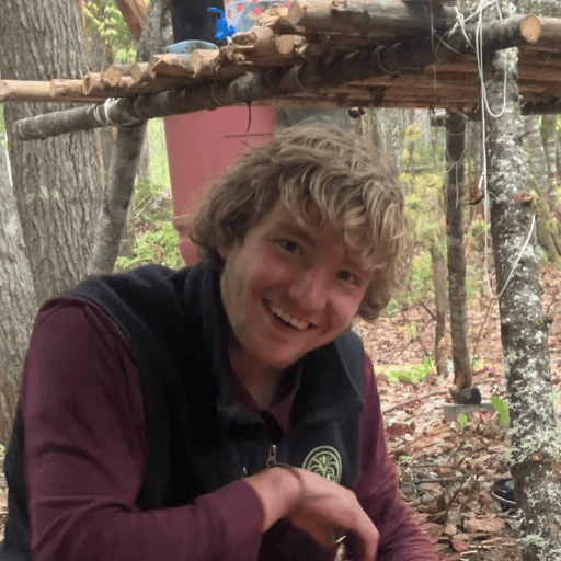 Young man smiling in a forest eco village environment with wooden structures.