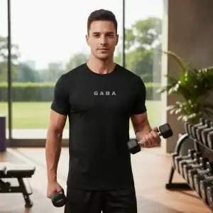 Man wearing GABA Performance Tee with dumbbells in gym setting.