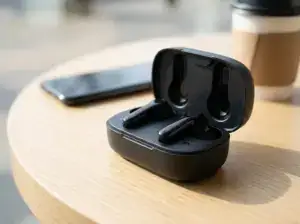 אוזניות אלחוטיות בתוך קופסת טעינה על שולחן עץ, ליד טלפון נייד וקפה, בסביבה מוארת באור טבעי.