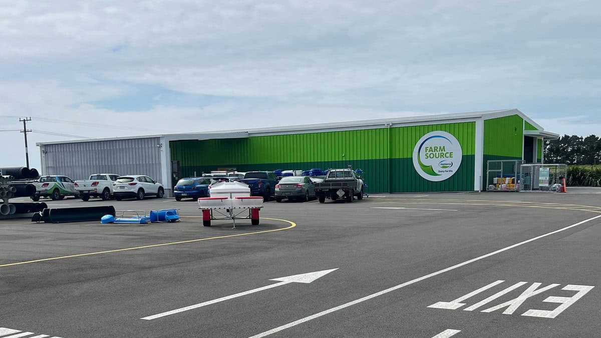 Bright green farm supply store with parked cars and outdoor equipment in a spacious parking lot.