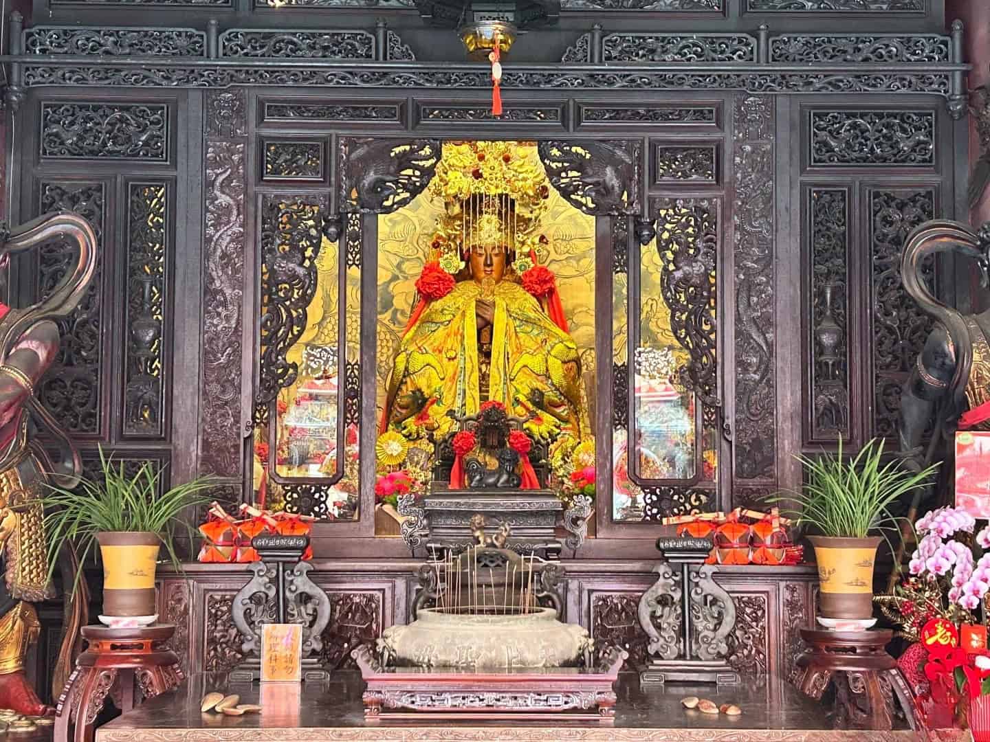 A Mazu statue on an altar in a Chinese ancestral hall, surrounded by offerings and decorations, reflecting Chinese genealogy and spiritual traditions.