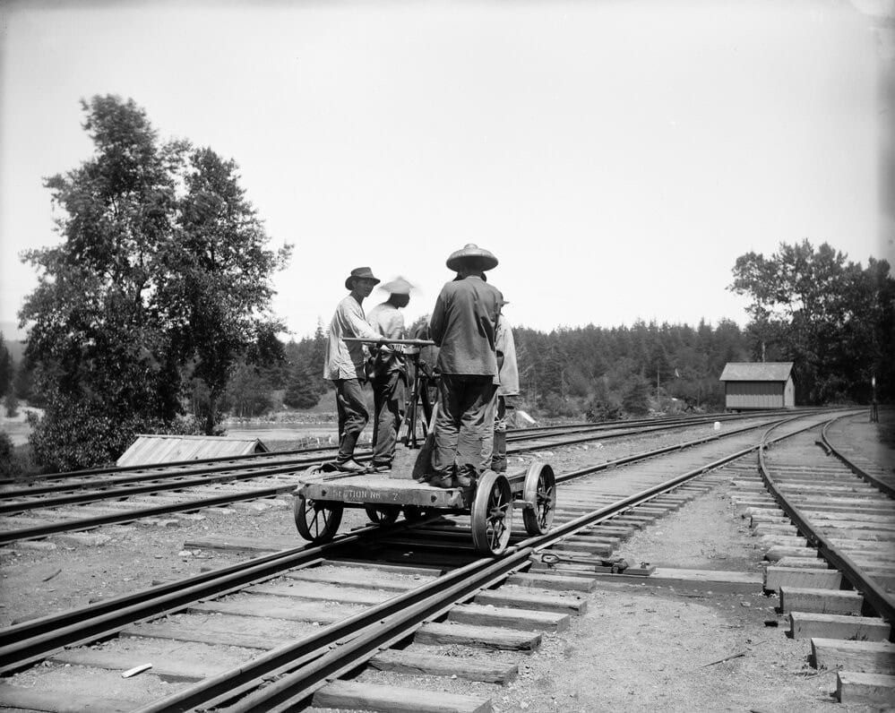 Chinese railroad workers standing on a handcart along the Northern Pacific Railway tracks, symbolizing their crucial role in shaping Montana’s infrastructure.