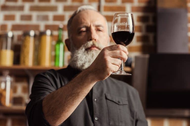 Bearded senior man looking at wine glass with red wine