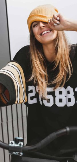 Sød kvinde med orange hue, iklædt streetwear, smilende og afslappet.