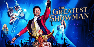 The Greatest Showman cast performing on stage with vibrant lights and audience in background.