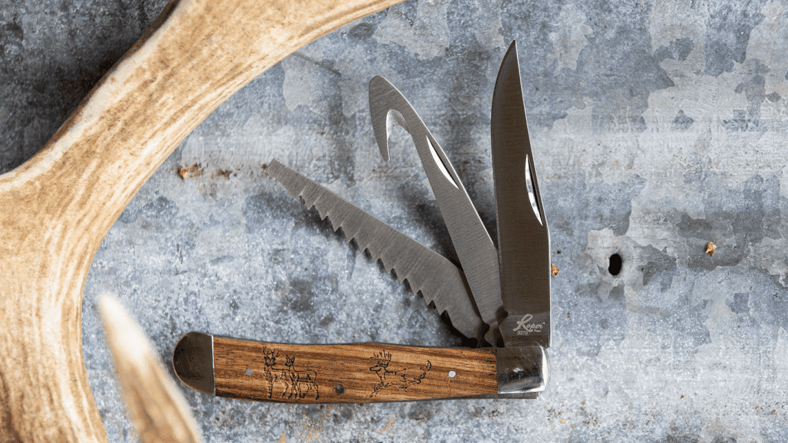 Roper multi-blade pocket knife by ABKT featuring a saw blade, gut hook, and traditional drop point blade. Wood handle with engraved deer scene.