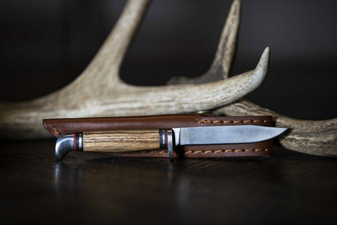 ABKT fixed blade hunting knife with a stacked wood handle and leather sheath, displayed in front of a deer antler.