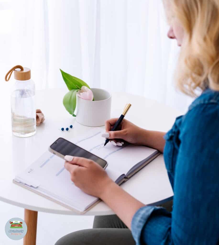lady holding her phone and writing in her notebook - benefits of goal setting