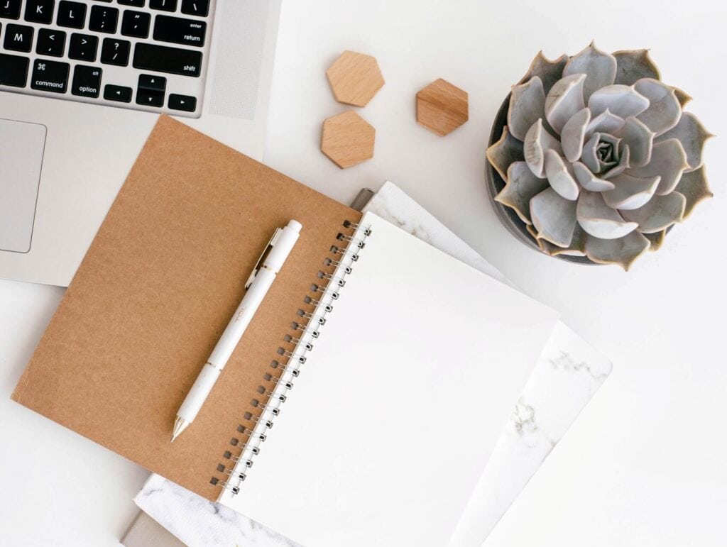 Minimalist desk featuring an open notebook with pen, laptop, and a succulent plant - how to blog consistently