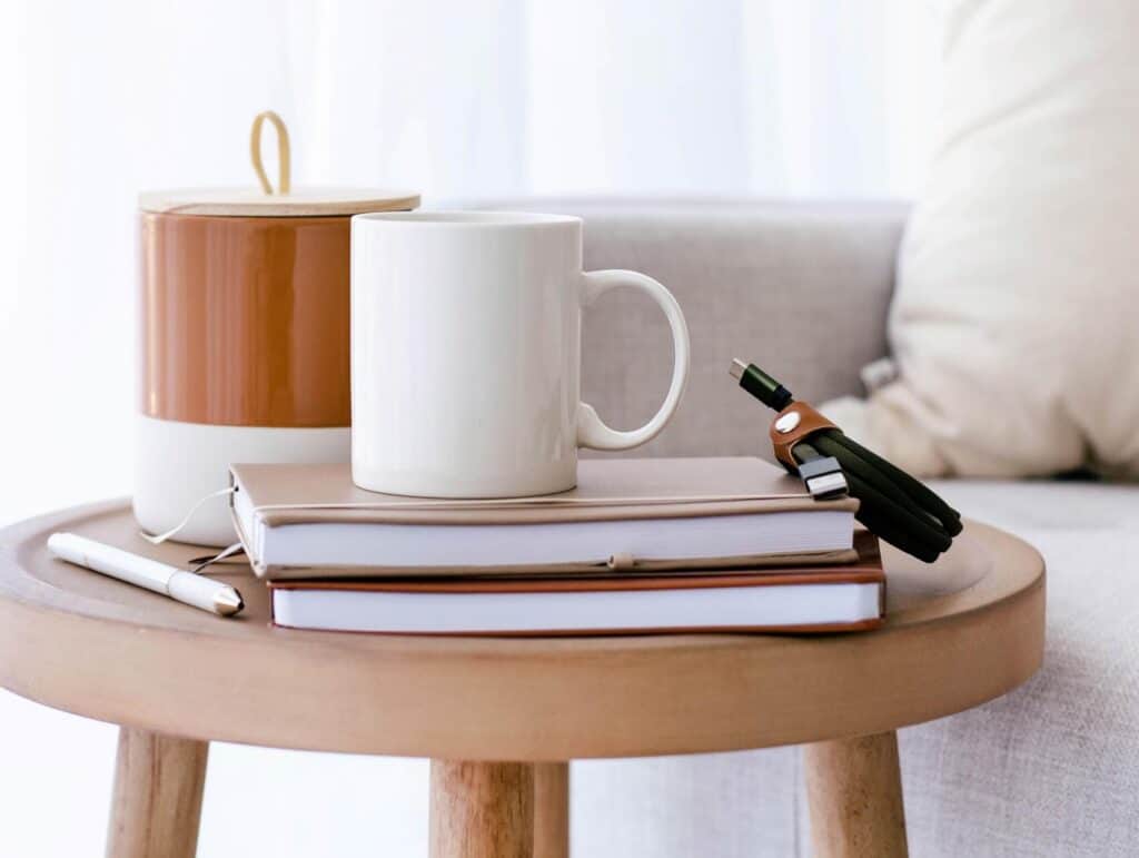 Steaming coffee mug and some notebooks on a wooden living room table before the couch - how to blog consistently