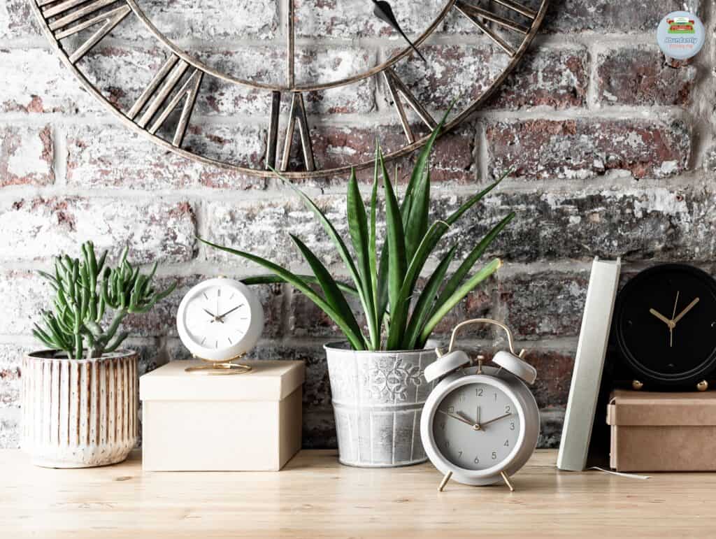 rustic wall with big metal analog clock, wooden side table, two plants, two boxes, and two analog alarm clocks - pomodoro technique