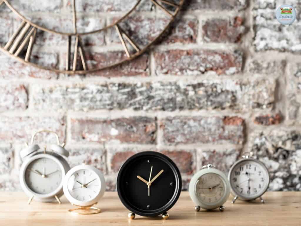 rustic wall with big metal analog clock, wooden side table, and 5 analog alarm clocks - pomodoro technique