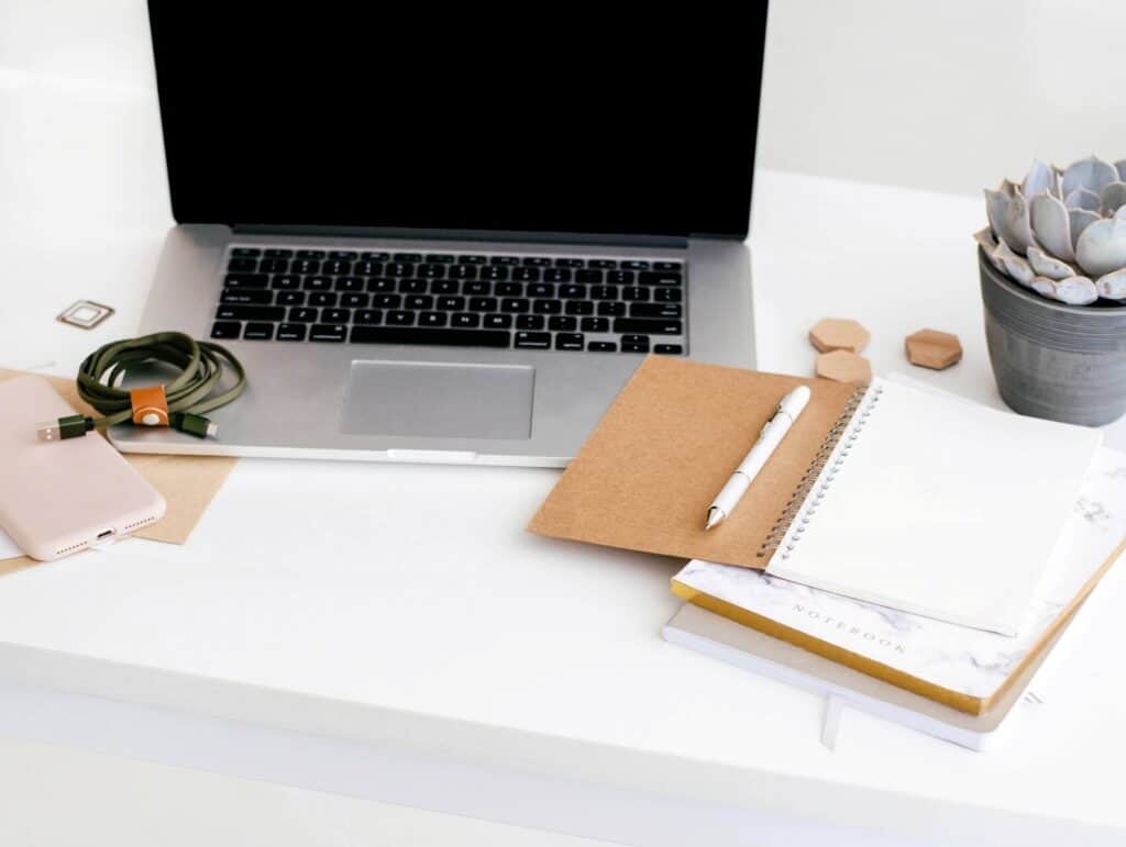 desk with open laptop, notebook and pen - how to blog consistently