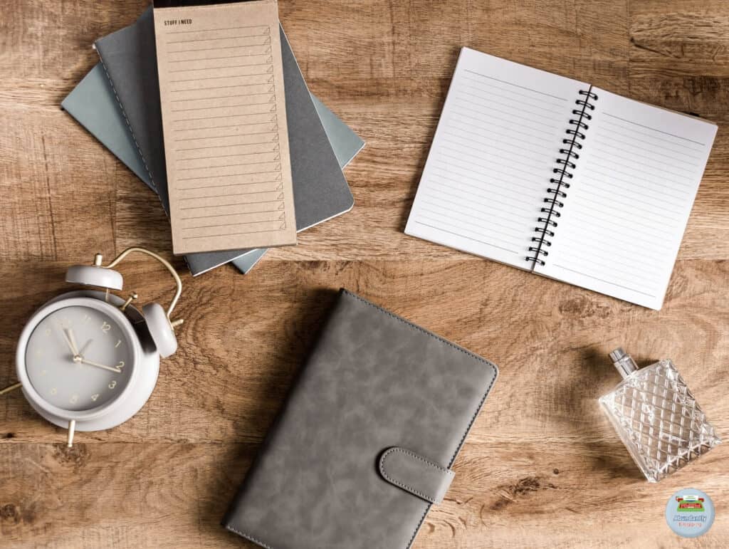 flatlay on wooden table with an analog alarm clock, and a few notebooks and notepads - Reasons for Procrastination