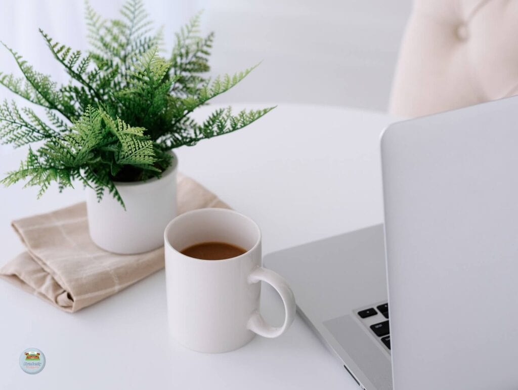 A white desk with an open laptop, a little plant and a cup of coffee. With the desk is a creme chair - 80/20 Rule in Blogging