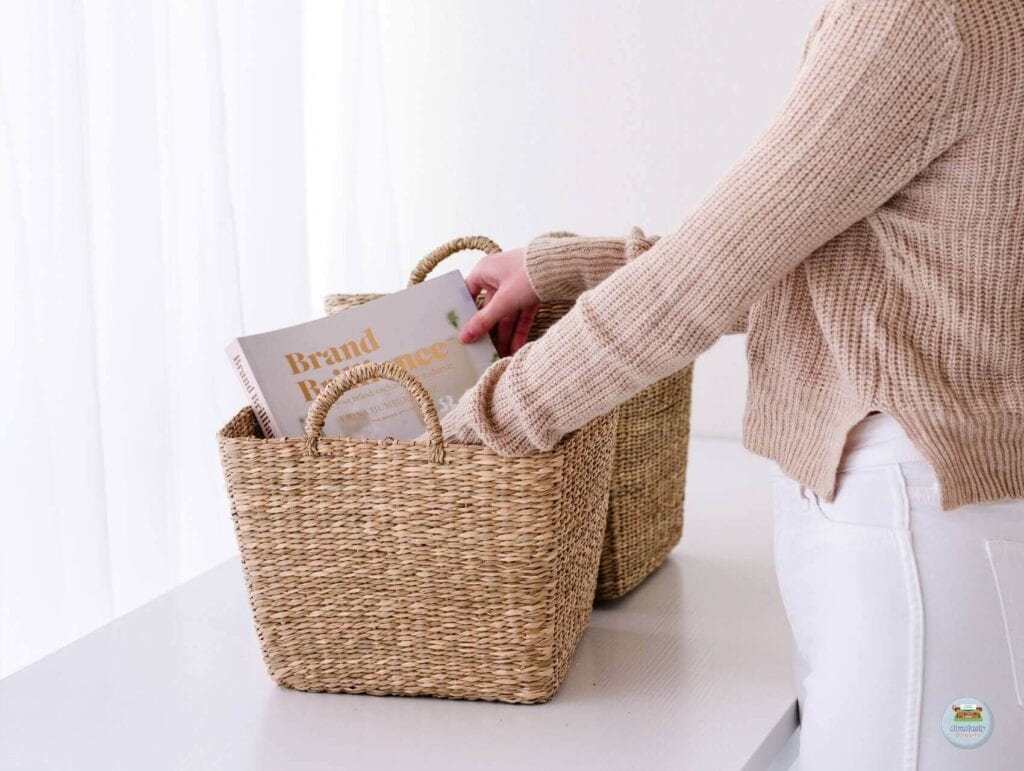 A white desk against the wall with 2 baskets and a woman going through one basket pulling out a book - 80/20 Rule in Blogging