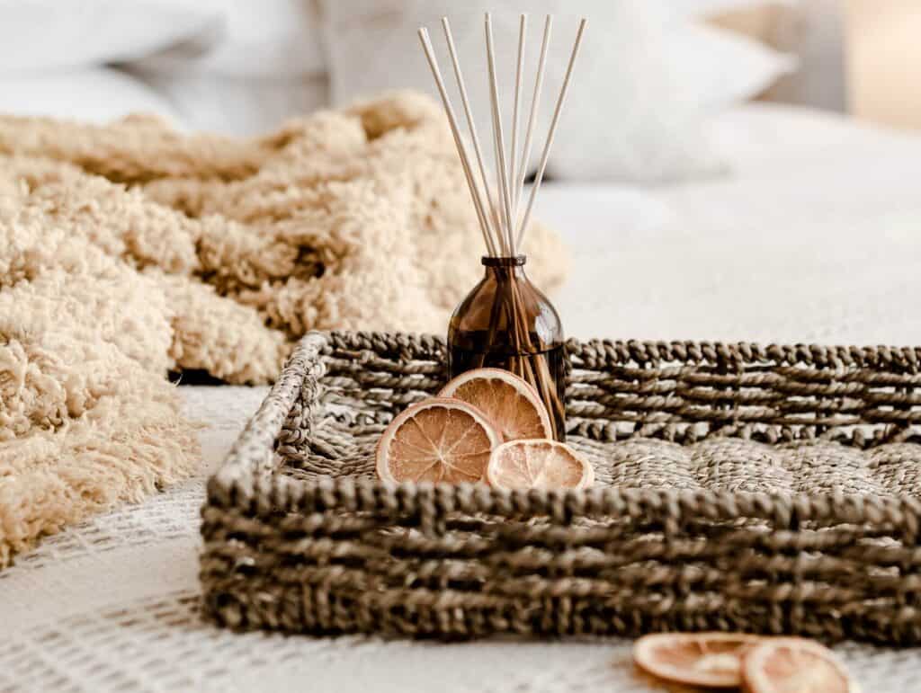 a cozy setting of a woven tray with dried orange slices and a bottle with scented sticks plus a throw blanket on a bed - evening routine ideas