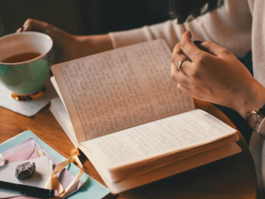 a woman sitting at her desk with her journal, a cup of tea and some sweets - evening routine ideas