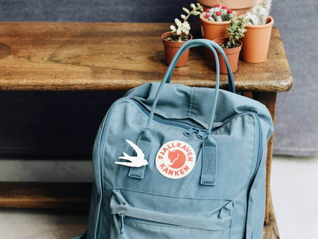 a Fjallraven backpack standing in a hallway against a wooden bench. On the bench are a few succulents in brown pots - evening routine ideas