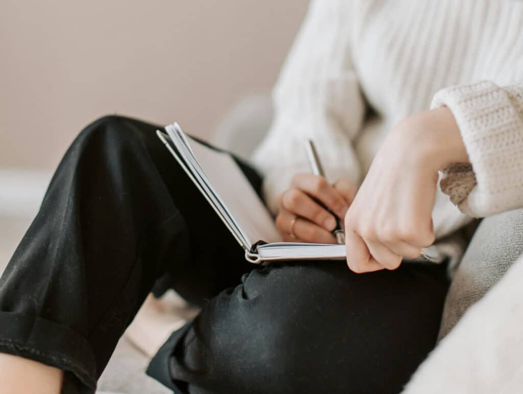 a woman sitting on the couch writing in her notebook - evening routine ideas
