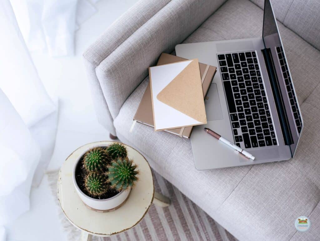 a topview of a modern grey couch. on it is an open laptop, a notebook, a card with envelop, and a pen. Beside the couch is a little table with a succulent on it - How to repurpose
