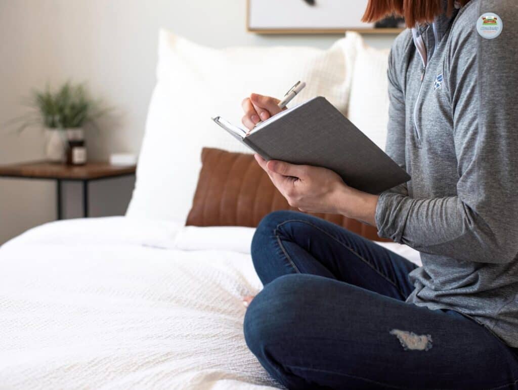 a woman sitting on her bed cross-legged writing in her notebook - How to repurpose