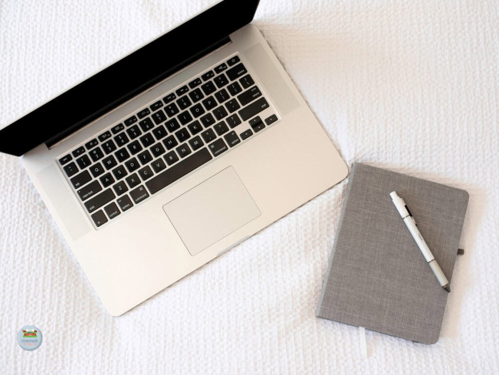 a flatlay of a open laptop and notebook with pen on a bed with white covers - How to repurpose